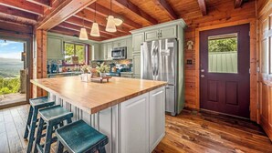 A kitchen with a large island, wooden ceiling beams, and a view of the outdoors.