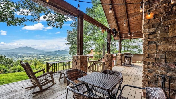 A wooden deck with wicker furniture and a stone wall, overlooking a scenic landscape.