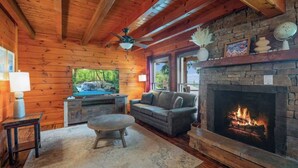 A cozy cabin interior with a stone fireplace, a television, and a comfortable seating area.