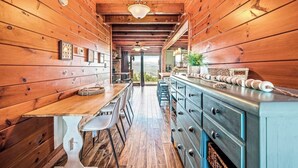 A wooden interior with a dining area, a kitchen counter, and a view through an open door.