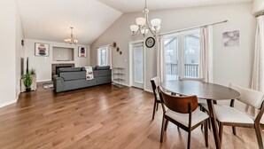 Ein geräumiges Wohnzimmer mit Holzboden, einem grauen Sofa, einem Esstisch mit Stühlen und einer Deckenleuchte.