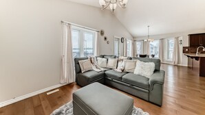 Ein geräumiges Wohnzimmer mit einer Eckcouch, einer Chandelüster und großen Fenstern.