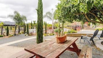 Ein Holztisch für ein Picknick mit einem Blumentopf, umgeben von einem Kiesweg und einem von Bäumen gesäumten, eingezäunten Bereich.