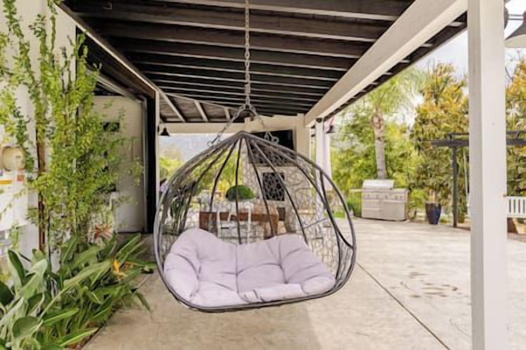 Ein Hängesessel mit Kissen, ein Betonboden und eine überdachte Terrasse mit Pflanzen.