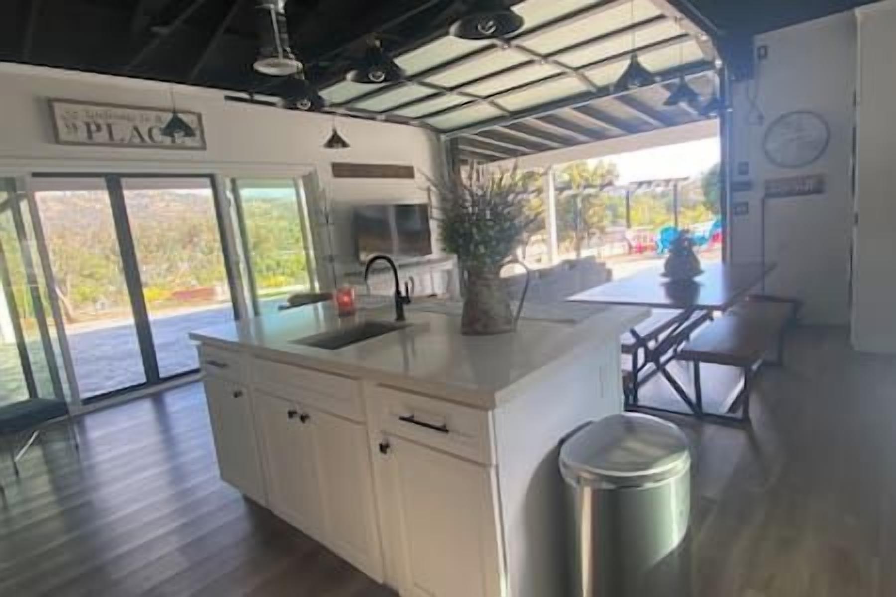 A kitchen with a large island, a sink, and a trash can. There is a dining area with a table and chairs.