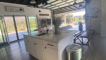 A kitchen with a large island, a sink, and a trash can. There is a dining area with a table and chairs.
