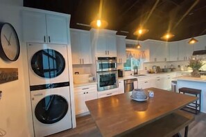 A modern kitchen with built-in appliances, a wooden dining table, and white cabinetry.
