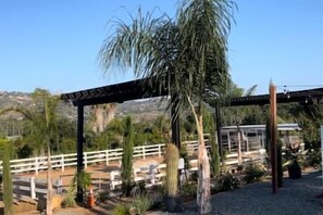 Ein überdachter Außenbereich mit einer Pergola, Palmen und einem weißen Zaun.