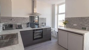A modern kitchen with a central island, built-in oven, and a large window. - Sunbeam House Apartment 3 (Morecambe)