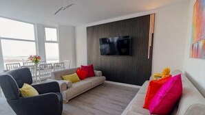 A modern living room with a sofa, armchair, and a flat-screen TV mounted on the wall. - Sunbeam House Apartment 3 (Morecambe)