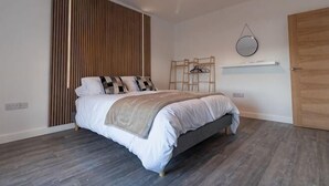 A bedroom with a bed, wooden slats, a hanging light fixture, a mirror, and a wooden door. - Sunbeam House Apartment 3 (Morecambe)