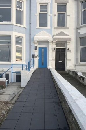 Un camino que lleva a un edificio con puerta azul, detalles blancos y un pequeño jardín.
