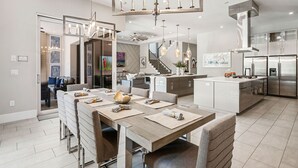 Eine moderne Küche mit Edelstahlgeräten, ein Essbereich mit einem langen Tisch und eine Treppe, die zu einer oberen Ebene führt.