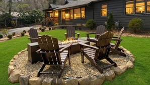 Une maison avec un foyer extérieur entouré de fauteuils Adirondack.