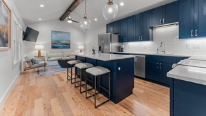 Une cuisine moderne avec des meubles de couleur bleu foncé, un îlot central doté de tabourets, des appareils en acier inoxydable et un éclairage suspendu.