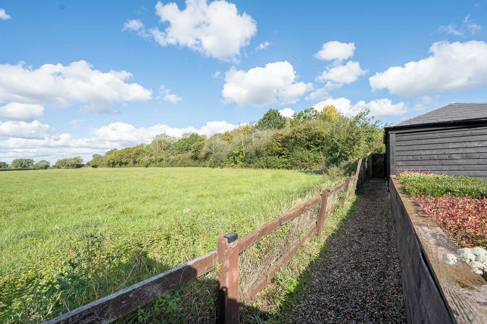 A wooden pathway leading to a building with a sloped roof, surrounded by a grassy field and trees.