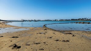 Une plage à l’eau d’un bleu limpide, avec un rivage sablonneux et un promontoire rocheux qui se dessine à l’horizon.
