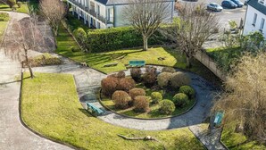 Un jardin circulaire agrémenté de divers arbustes et d’un banc, entouré d’un chemin pavé et avec un bâtiment visible au loin.