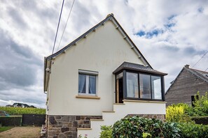 Une maison de plain-pied avec un toit à pignon, une petite fenêtre avec des rideaux et des fondations en pierre.