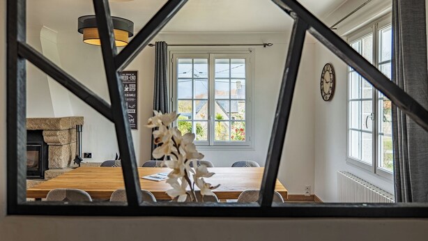 Een eethoek met een houten tafel en stoelen, een open haard en een uitzicht door een geometrisch raam.