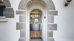 Een stenen boogpoort leidt naar een modern interieur met een houten vloer en uitzicht op de omgeving.
