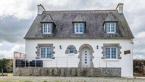 Een huis met twee verdiepingen, een gevel van natuursteen, meerdere ramen en een stenen muur ervoor.