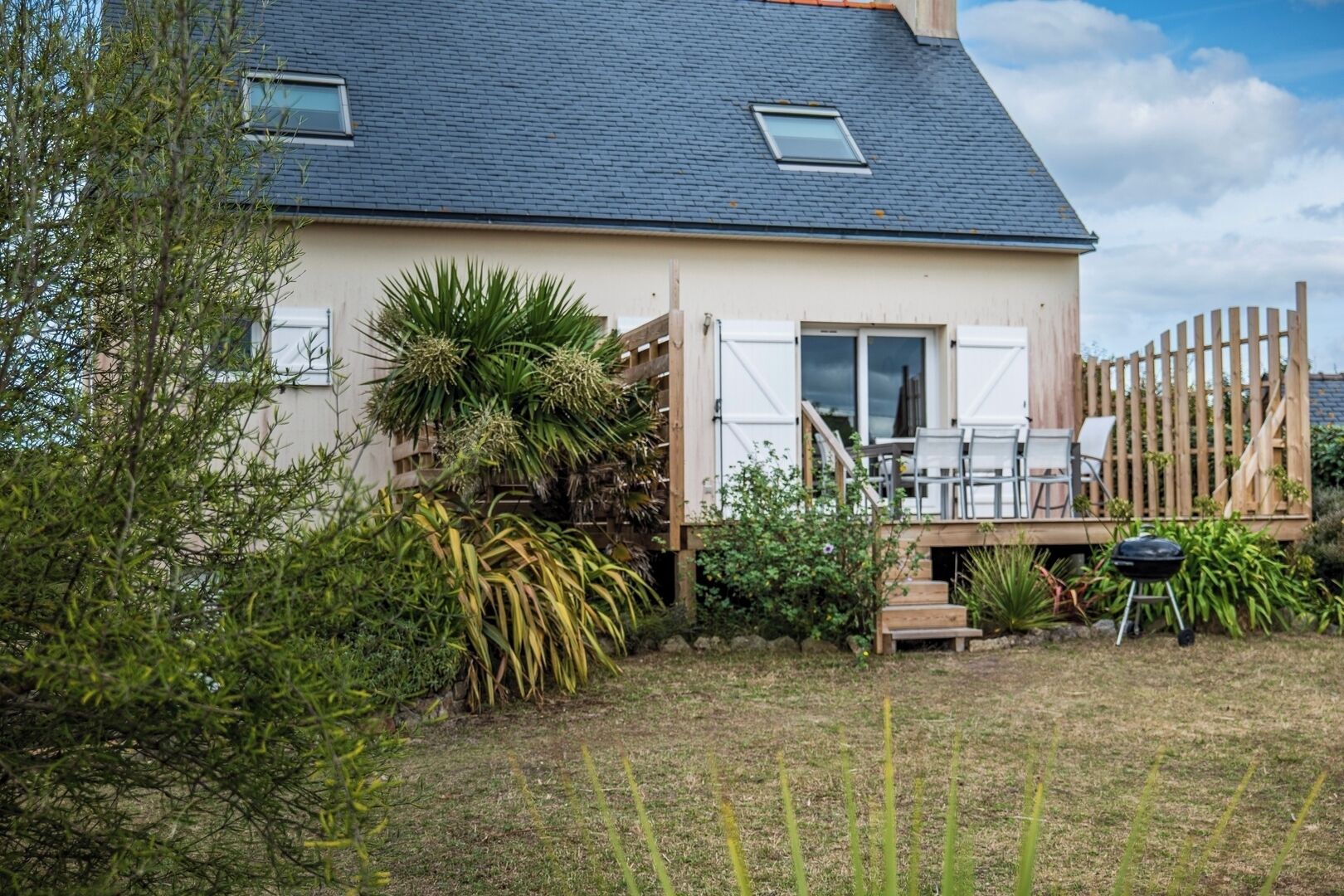 A house with a sloped roof, a deck with outdoor furniture, and a garden with various plants.
