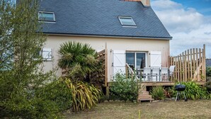 Una casa con tetto spiovente, un patio con mobili da esterno e un giardino con diverse piante.