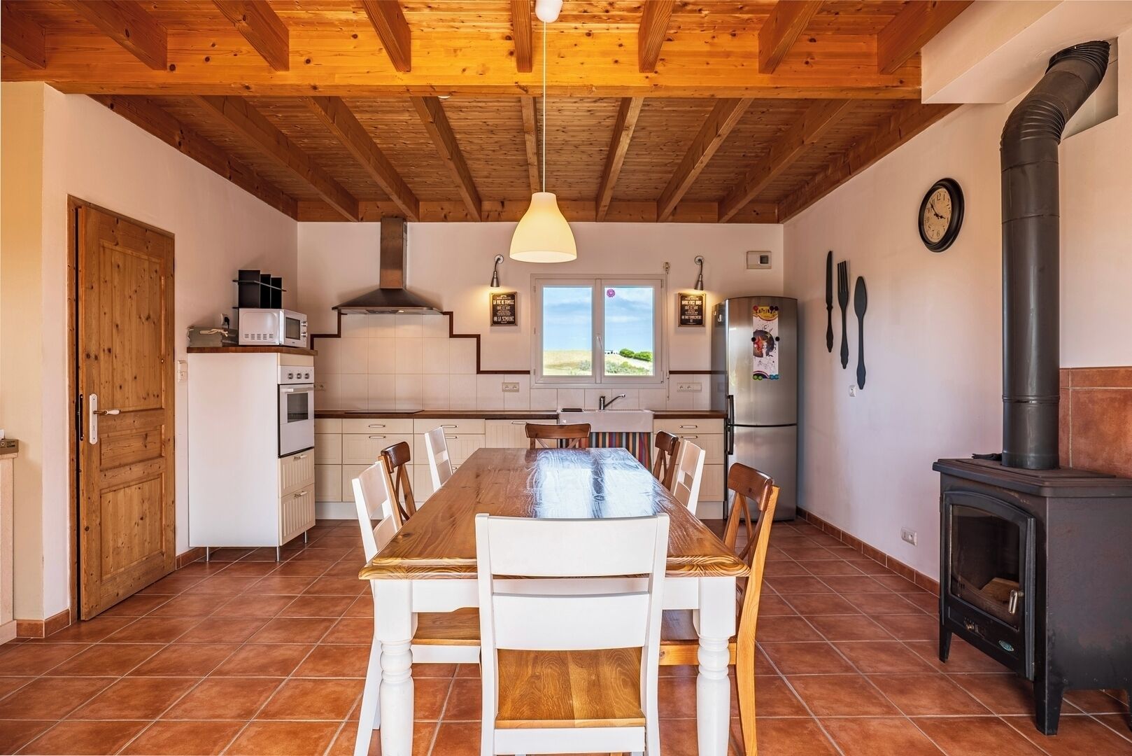 A kitchen with a wooden table, chairs, a stove, and a window with a view.