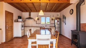 A kitchen with a wooden table, chairs, a stove, and a window with a view.