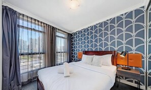 Hotellihuone, jossa on suuri sänky, yöpöytä lampun kanssa ja näkymä ikkunasta.