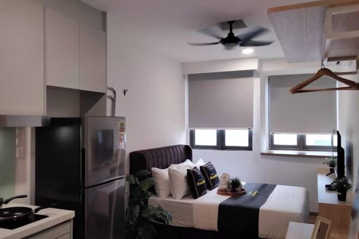 A modern hotel room with a bed, a refrigerator, a ceiling fan, and a window with a view.