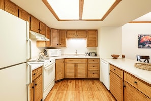 A kitchen with wooden cabinets, a white refrigerator, a microwave, a stove, and a sink.