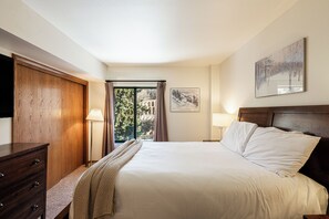 Una camera da letto con un letto, un armadio in legno, una finestra con tende e un quadro appeso al muro.