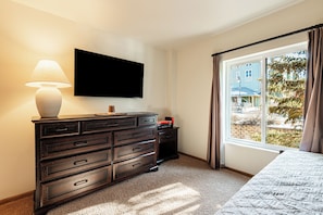 A bedroom with a TV mounted on the wall, a dresser, a bed, and a window with curtains.
