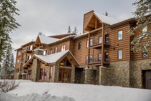 A multi-story lodge with stone foundations and wooden exterior, featuring balconies and large windows.