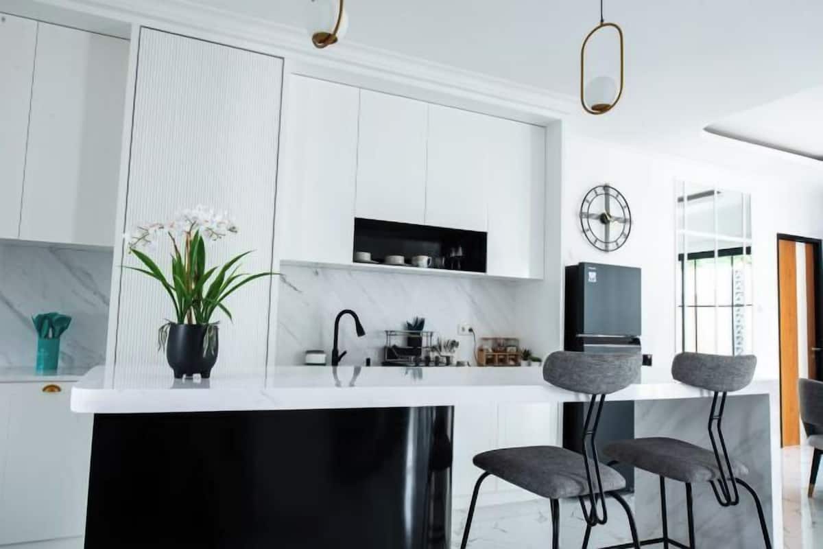 A modern kitchen with white cabinets, a black countertop, and a bar area with grey stools.
