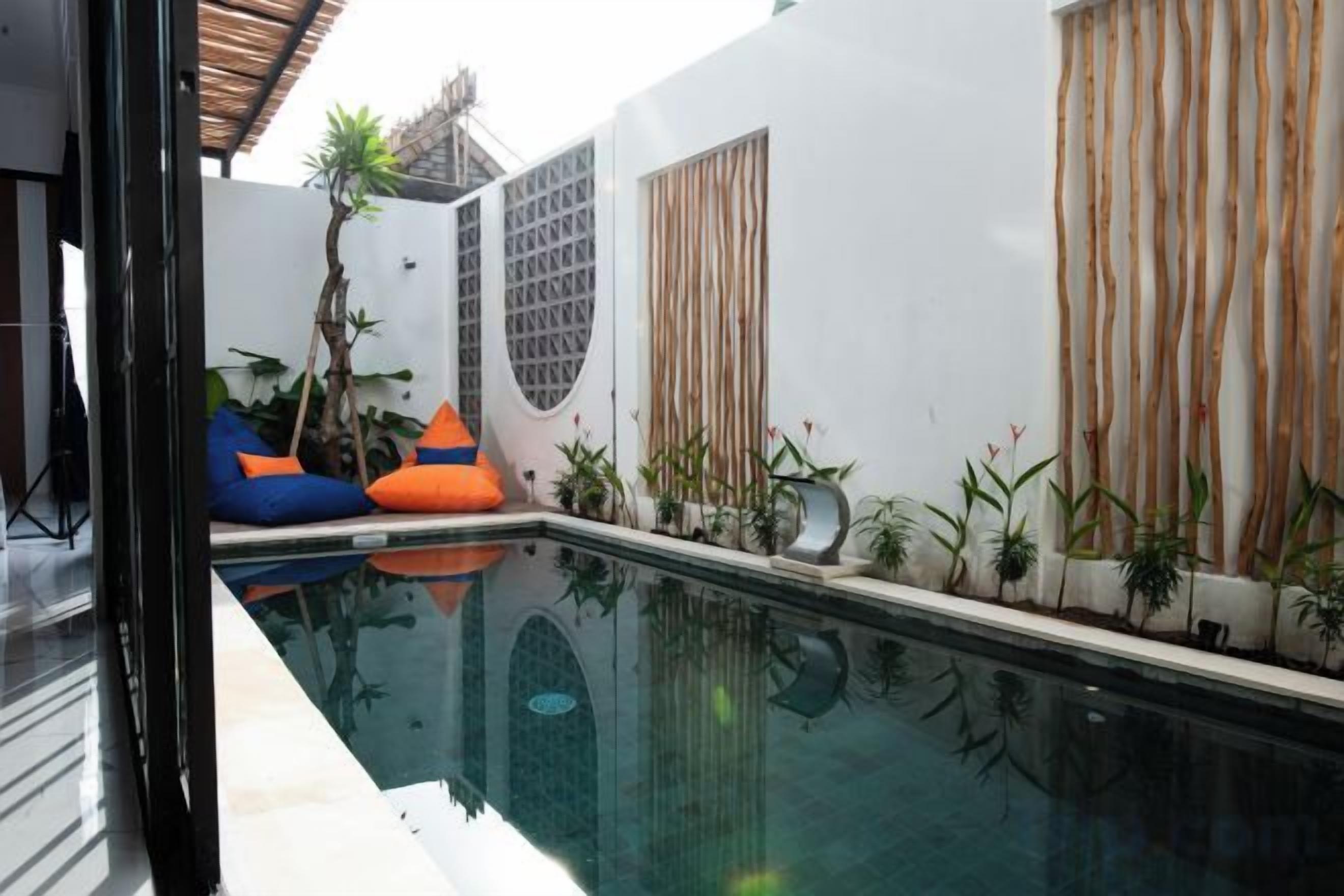 A swimming pool with a clear view of the water, surrounded by potted plants and a white wall with a window.