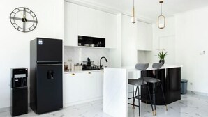 A modern kitchen with a black refrigerator, a water dispenser, a marble countertop, and a bar area with stools. - Inori Villas (Bali)