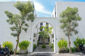 Une entrée en arc, agrémentée de plantes en pot de chaque côté, qui mène à un bâtiment à la façade blanche.