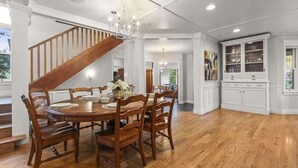 A dining area with a wooden table and chairs, a staircase, and a white cabinet with glass doors.