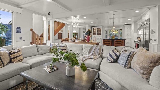 A spacious living room with a large sofa, a coffee table, and a dining area in the background.