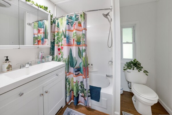 A bathroom with a white sink, a mirror, a shower curtain with a plant pattern, a toilet, and a window.