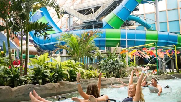 Parque acuático interior con un tobogán de agua grande, flotadores hinchables y abundante vegetación.