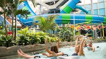 An indoor water park with a large water slide, inflatable tubes, and lush greenery.