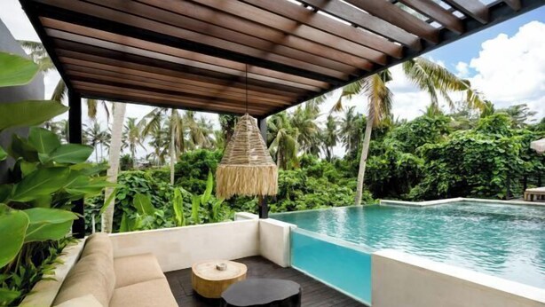 Un área junto a la piscina con un muelle de madera, una sombrilla de paja y una zona de estar acolchada.