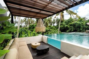 Un área junto a la piscina con un muelle de madera, una sombrilla de paja y una zona de estar acolchada.