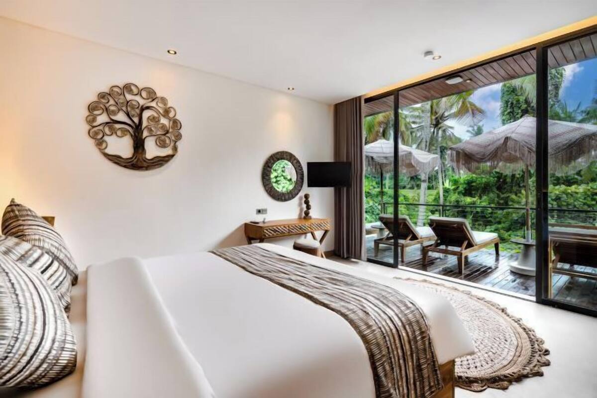 A bedroom with a large bed, a wall-mounted TV, a clock, and a view of a deck with outdoor furniture.