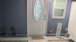 A house with a grey door, a welcome sign, and a small garden with potted plants.