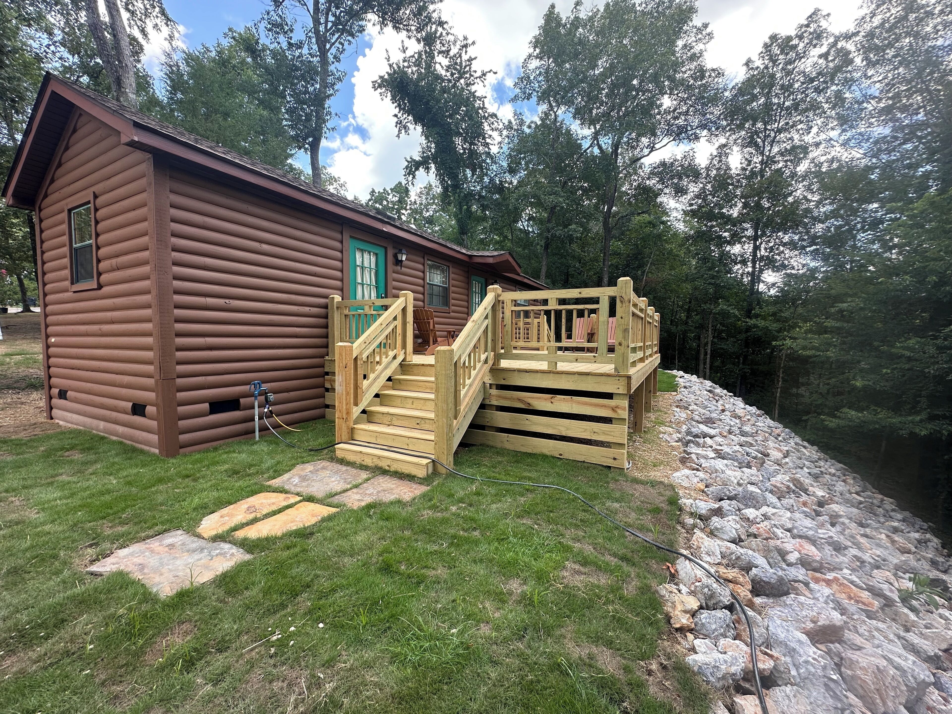 A log cabin with a wooden deck and a stone pathway leading to a dock.